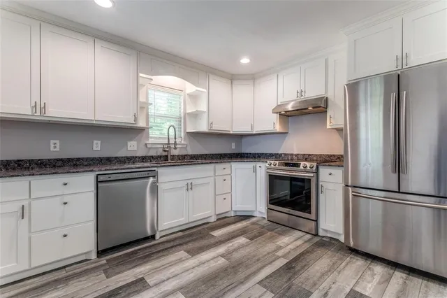 a kitchen with granite countertop white cabinets stainless steel appliances and a window