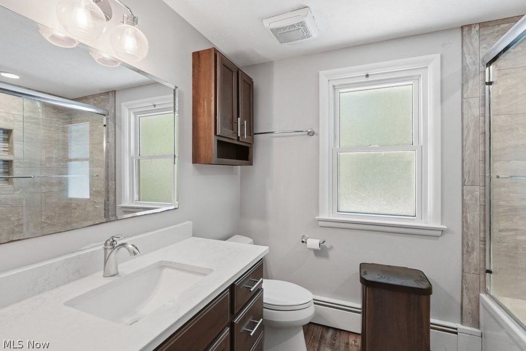 136 Pinehurst Road Munroe Falls, OH 44262 - Photo 27 of 48 Bathroom featuring a single vanity with a white countertop and a rectangular undermount sink, dark wood-finish cabinetry, a glass-enclosed shower with tile surround, and wood-finish flooring