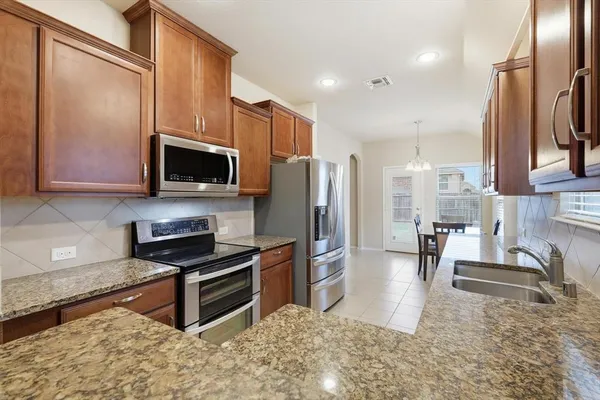 a kitchen with stainless steel appliances granite countertop a refrigerator a stove and a sink with wooden cabinets