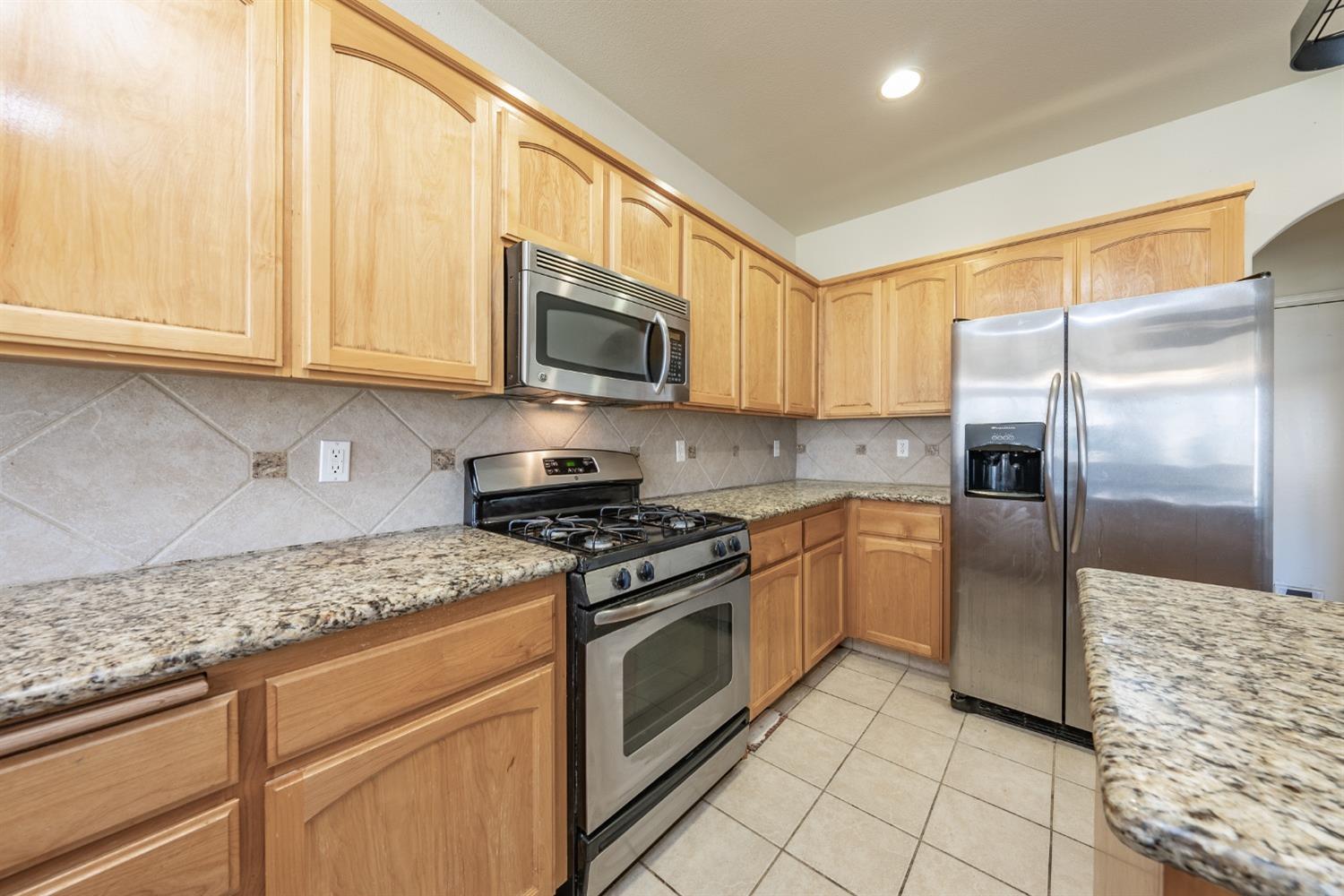 2727 Pear Tree Drive Madera, CA 93637 - Photo 11 of 36 a kitchen with granite countertop a refrigerator a stove top oven and cabinets