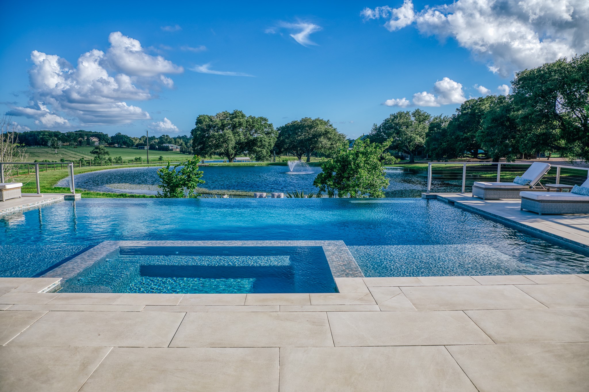 1034 Hilbun Road New Ulm, TX 78950 - Photo 12 of 49 Resort-style outdoor living featuring a negative-edge infinity pool overlooking a stocked pond, expansive covered patio, outdoor kitchen, and breathtaking views of the surrounding countryside.