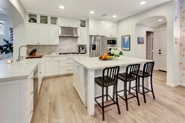 a kitchen with stainless steel appliances granite countertop a stove a sink a refrigerator and white cabinets with wooden floor