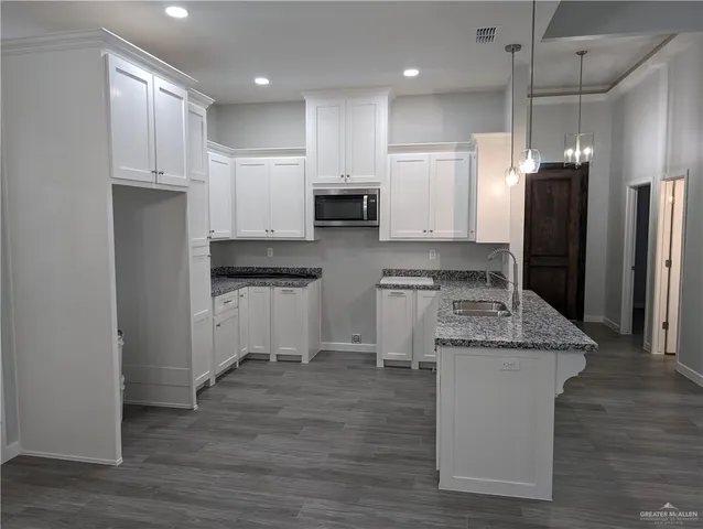 a kitchen with kitchen island granite countertop a refrigerator a oven a sink and white cabinets with wooden floor
