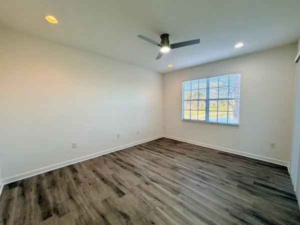 an empty room with wooden floor ceiling fan and windows