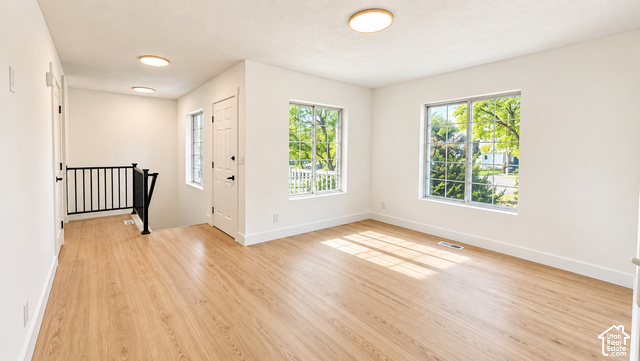 342 East 600 North Logan, UT 84321 - Photo 4 of 19 Spacious room featuring wood-finish flooring, multiple windows, a white paneled door, and a black metal staircase railing