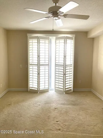 an empty room with chandelier fan and windows
