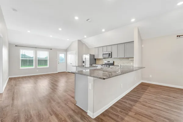 a large kitchen with stainless steel appliances granite countertop a large counter top a wooden floors and a large window