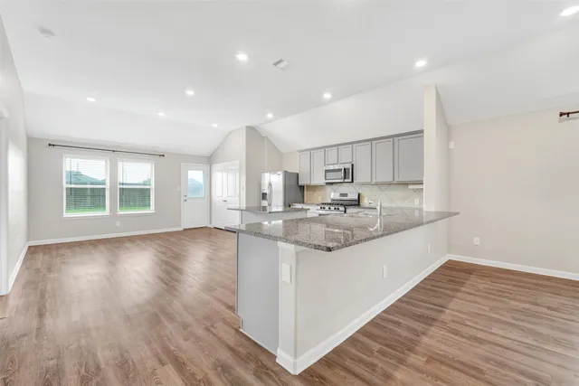 a large kitchen with stainless steel appliances granite countertop a large counter top a wooden floors and a large window