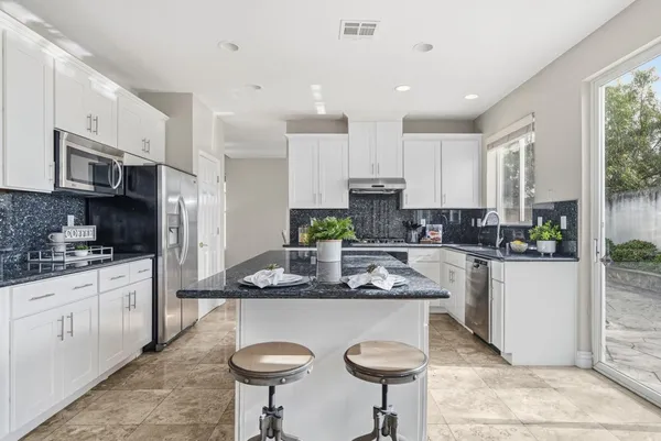 a kitchen with stainless steel appliances kitchen island granite countertop a sink a stove a refrigerator cabinets and chairs