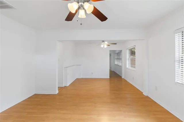 an empty room with chandelier fan and windows