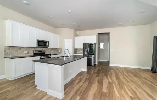 a large kitchen with granite countertop a stove top oven a sink dishwasher and a refrigerator with wooden floor