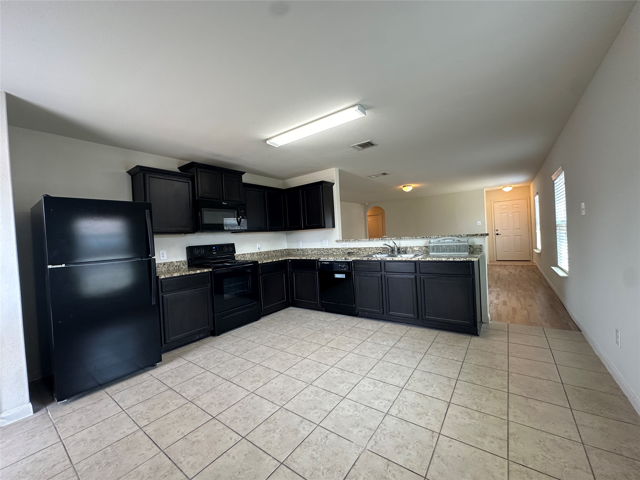 104 Millers Loop Jarrell, TX 76537 - Photo 5 of 11 The kitchen features dark cabinetry, granite-style countertops, and a full suite of black appliances, including a refrigerator, oven, and dishwasher