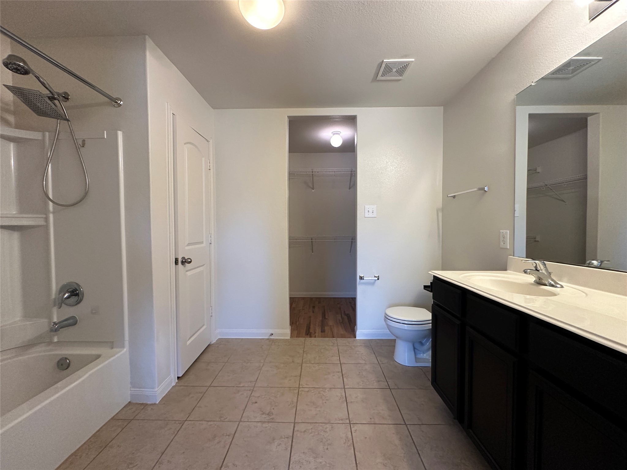 104 Millers Loop Jarrell, TX 76537 - Photo 8 of 11 The bathroom features a combination tub and shower with a handheld showerhead, a toilet, and a vanity with a single sink and dark cabinetry