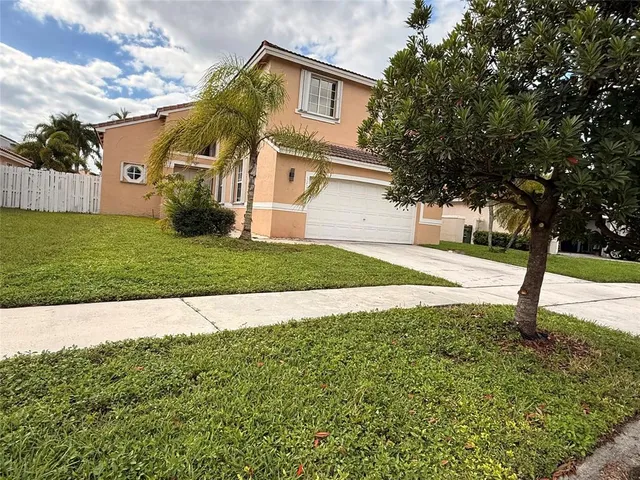 a view of a white house with a small yard and a large tree