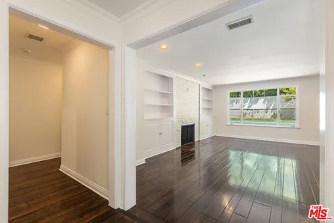 a view of an empty room with wooden floor fireplace and a window
