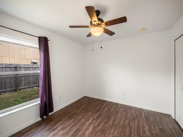 an empty room with wooden floor fan and windows