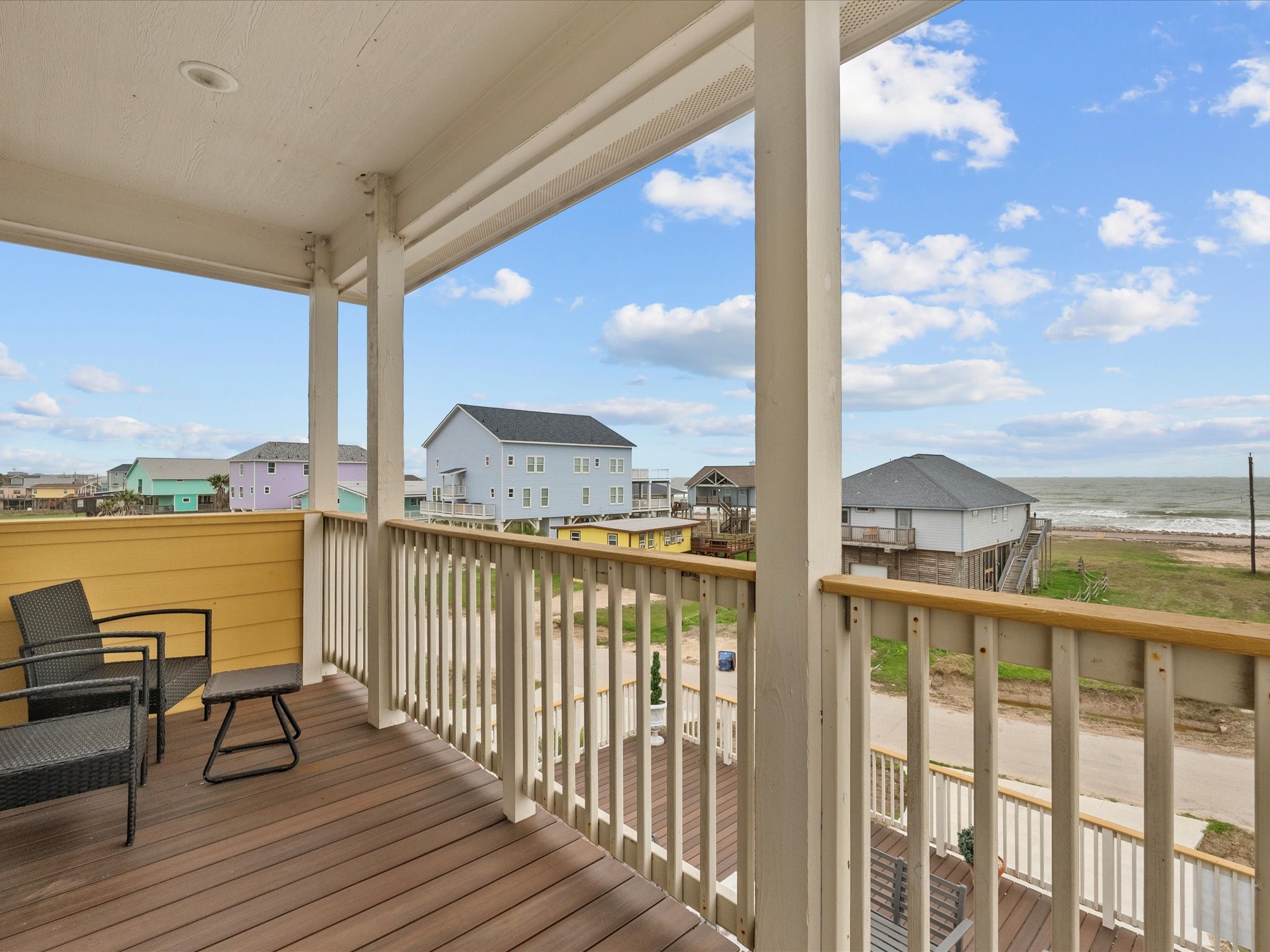 1018 Seashell Drive Surfside Beach, TX 77541 - Photo 46 of 49 This photo showcases a covered balcony with seating, offering a serene view of the ocean and nearby beach houses, perfect for enjoying coastal living.