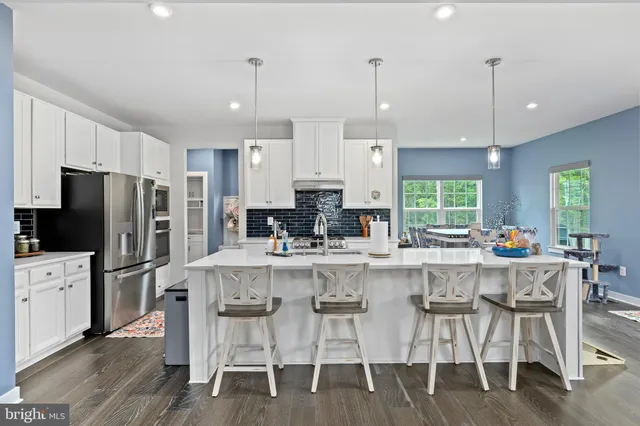 a kitchen with stainless steel appliances kitchen island granite countertop a stove a refrigerator a oven a sink with island chairs and wooden floor
