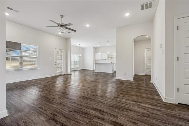 an empty room with wooden floor ceiling fan and kitchen view