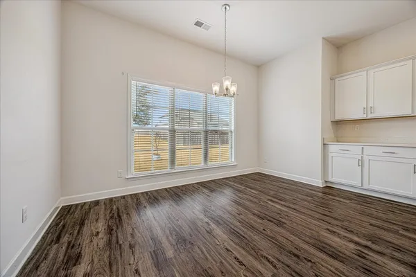 an empty room with wooden floor ceiling fan and kitchen view