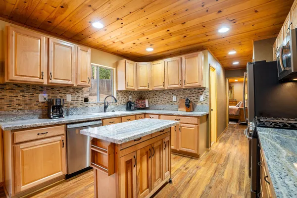 a kitchen with stainless steel appliances granite countertop wooden cabinets a sink dishwasher a stove and a refrigerator with wooden floor