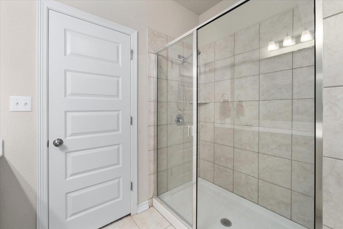 5408 Vanner Path Georgetown, TX 78626 - Photo 20 of 34 Glass-enclosed shower with tile surround and integrated shelving, featuring a multi-panel interior door with brushed nickel hardware