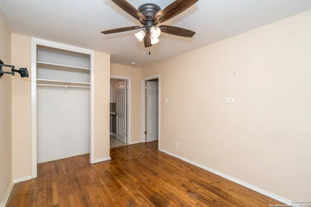 a view of an empty room with window a ceiling fan and wooden floor