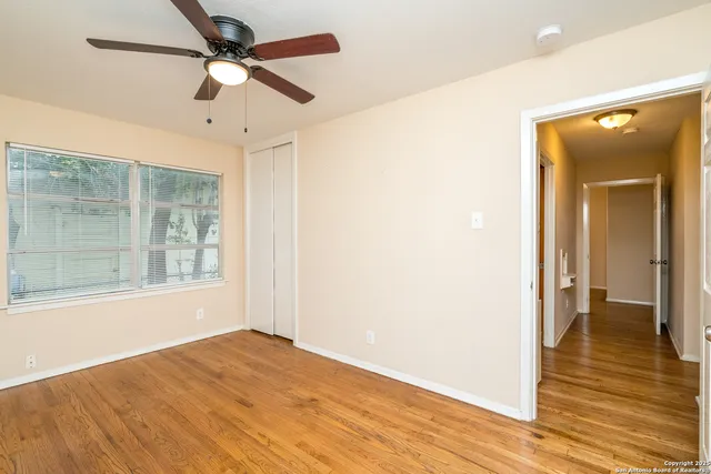 a view of empty room with wooden floor and fan