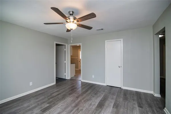 an empty room with wooden floor fan and windows