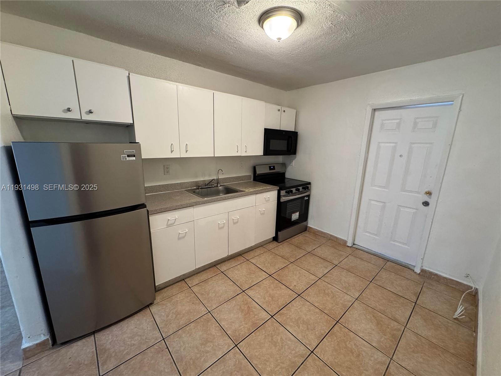 2146 Northwest 18th Terrace, Unit B Miami, FL 33125 - Photo 17 of 19 a kitchen with a refrigerator sink and cabinets