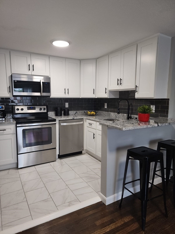 99 Cluff Crossing Road, Unit B12 Salem, NH 03079 - Photo 11 of 12 a kitchen with stainless steel appliances a stove a sink a microwave and wooden cabinets