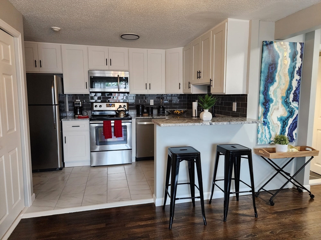 99 Cluff Crossing Road, Unit B12 Salem, NH 03079 - Photo 9 of 12 a kitchen with stainless steel appliances wooden floors and wooden cabinets