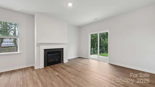 an empty room with wooden floor fireplace and windows