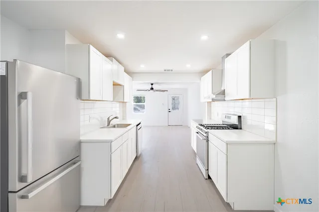 a kitchen with a sink a stove a refrigerator and white cabinets