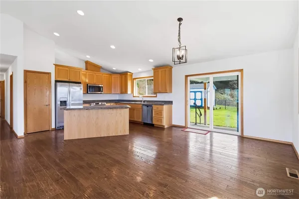 a view of kitchen with stainless steel appliances granite countertop a refrigerator a stove top oven a sink and a wooden floor