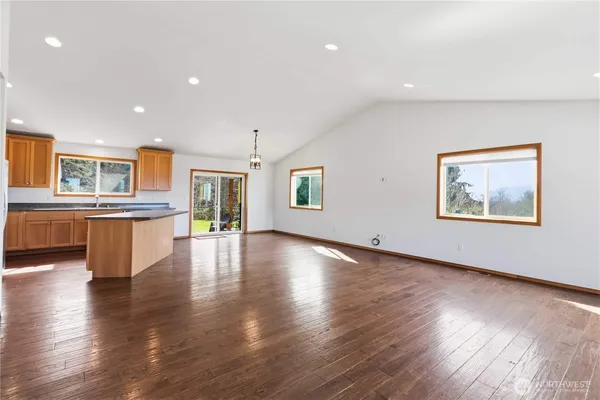a view of an empty room with wooden floor and a kitchen