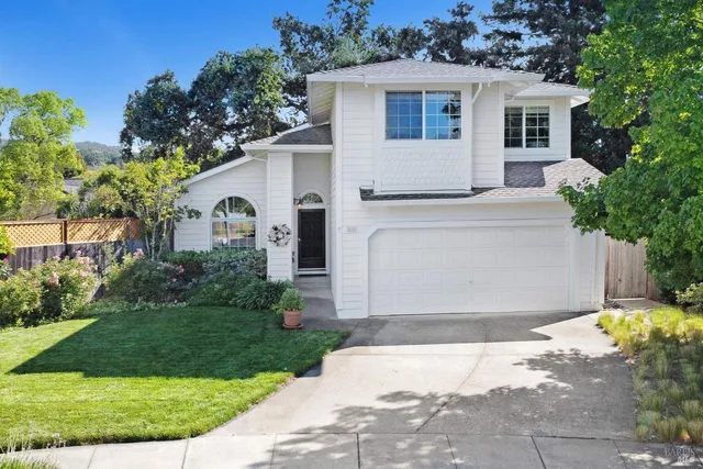 a view of a white house with a small yard and large trees