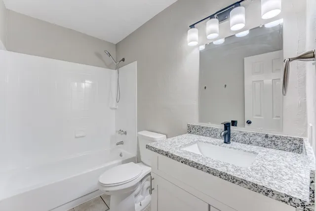 a bathroom with a granite countertop sink a toilet a mirror and shower
