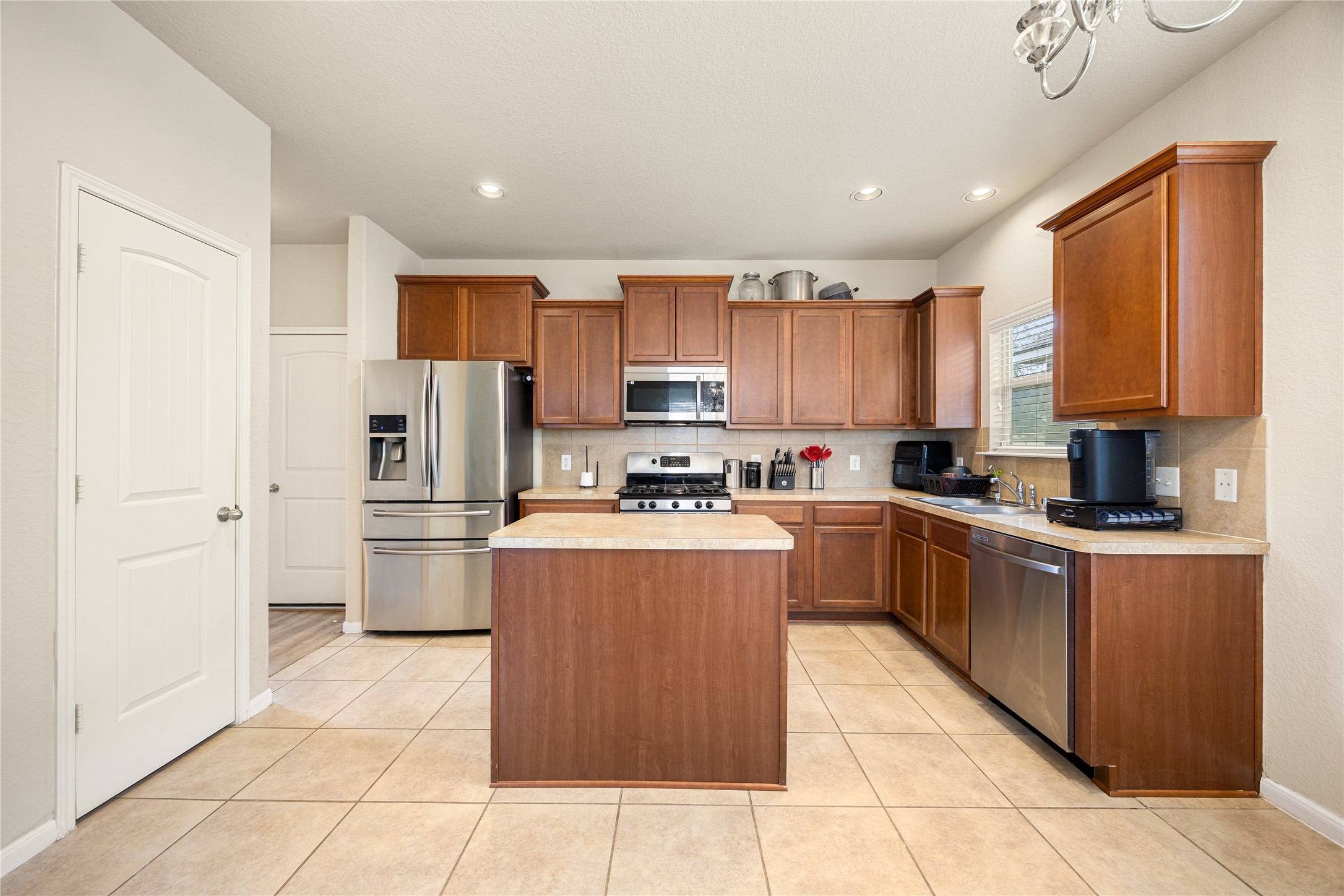 3526 Canvasback Lane Houston, TX 77047 - Photo 9 of 22 The spacious kitchen offers a functional and inviting design, featuring dark-stained wood cabinetry, granite countertops, stainless steel appliances, a tile backsplash, recessed lighting, and a center island providing additional prep space. Large windows bring in natural light, while the pantry adds convenient storage making this kitchen ideal for everyday cooking and entertaining.