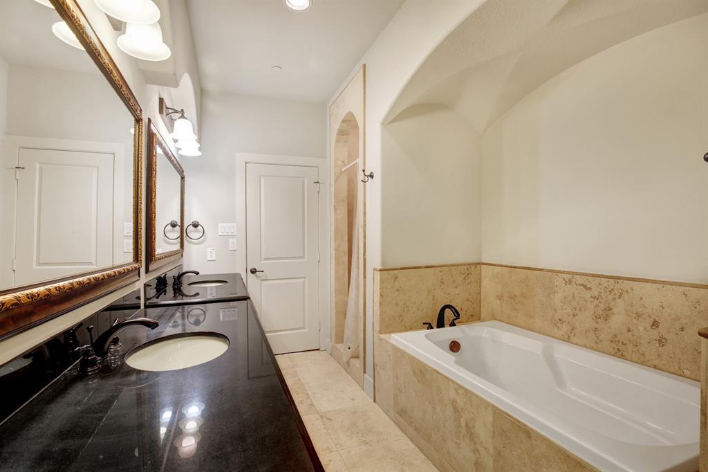 4111 Rawlins Street, Unit 403 Dallas, TX 75219 - Photo 18 of 23 Bathroom featuring a built-in tub with natural stone surround, a dual vanity with a dark countertop and undermount sinks, and an arched ceiling detail