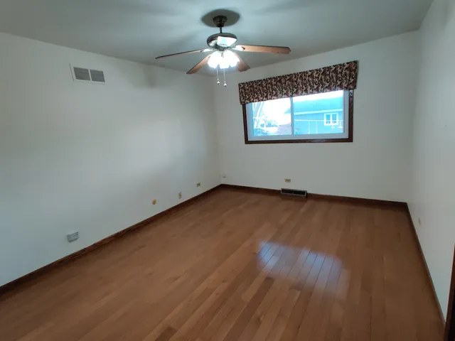 an empty room with wooden floor chandelier fan and windows