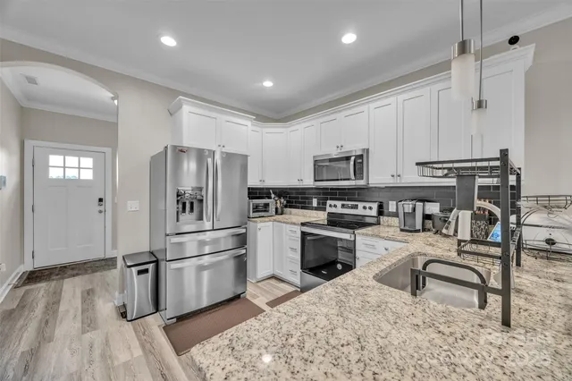 a kitchen with granite countertop a refrigerator a sink dishwasher a stove and white cabinets with wooden floor