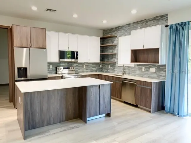 a kitchen with stainless steel appliances a stove top oven a sink dishwasher a refrigerator and a oven with wooden floor