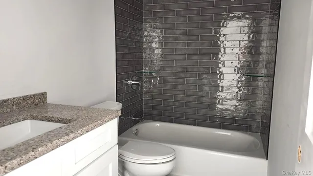 a bathroom with a granite countertop bathtub shower sink vanity and toilet