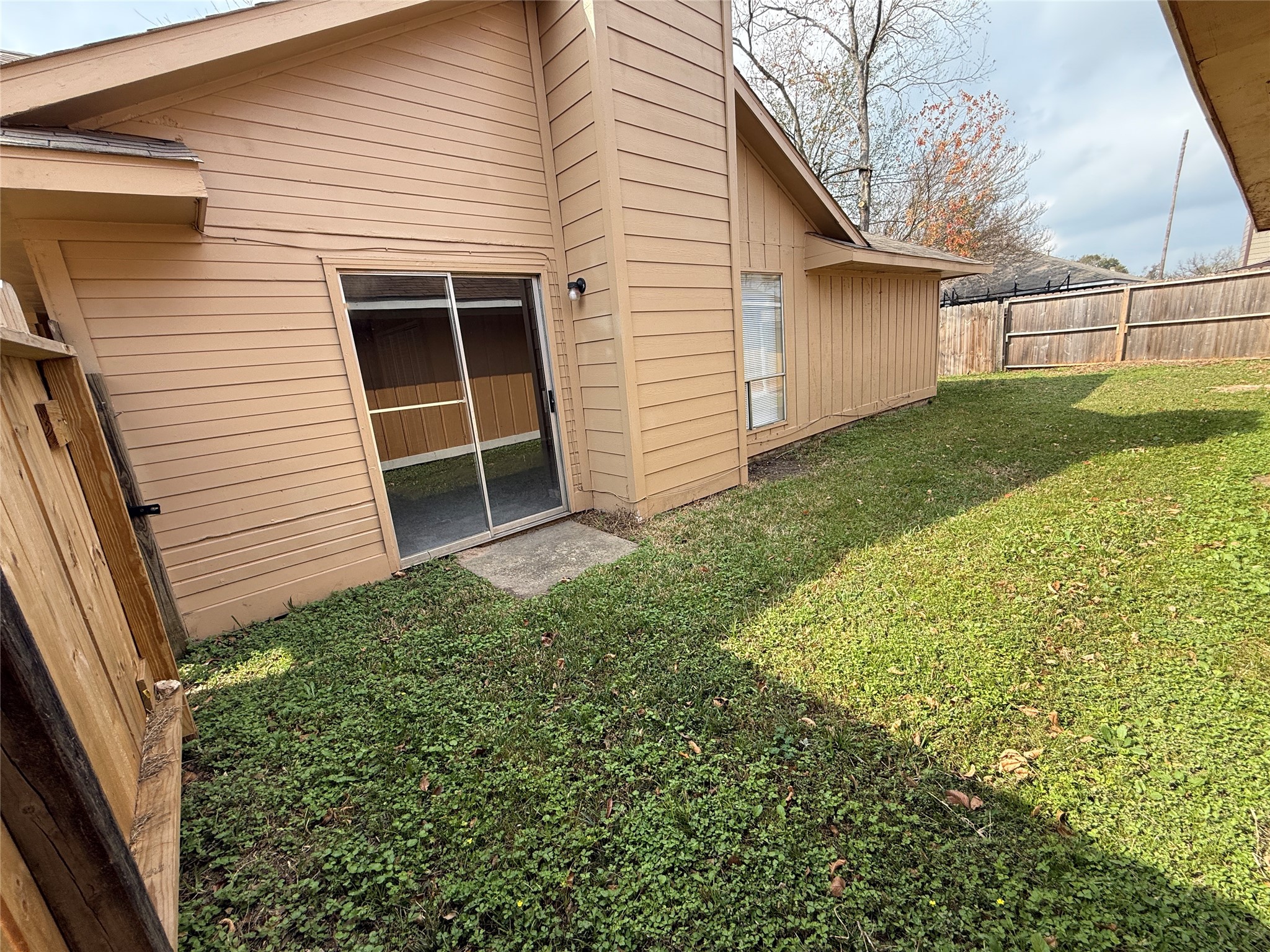 3219 Forestbrook Drive Spring, TX 77373 - Photo 14 of 16 Side/backyard with a well-maintained grassy area and a wooden fence for privacy. There's a sliding glass door that leads into the living area. Ideal for enjoying outdoor space in a compact setting.