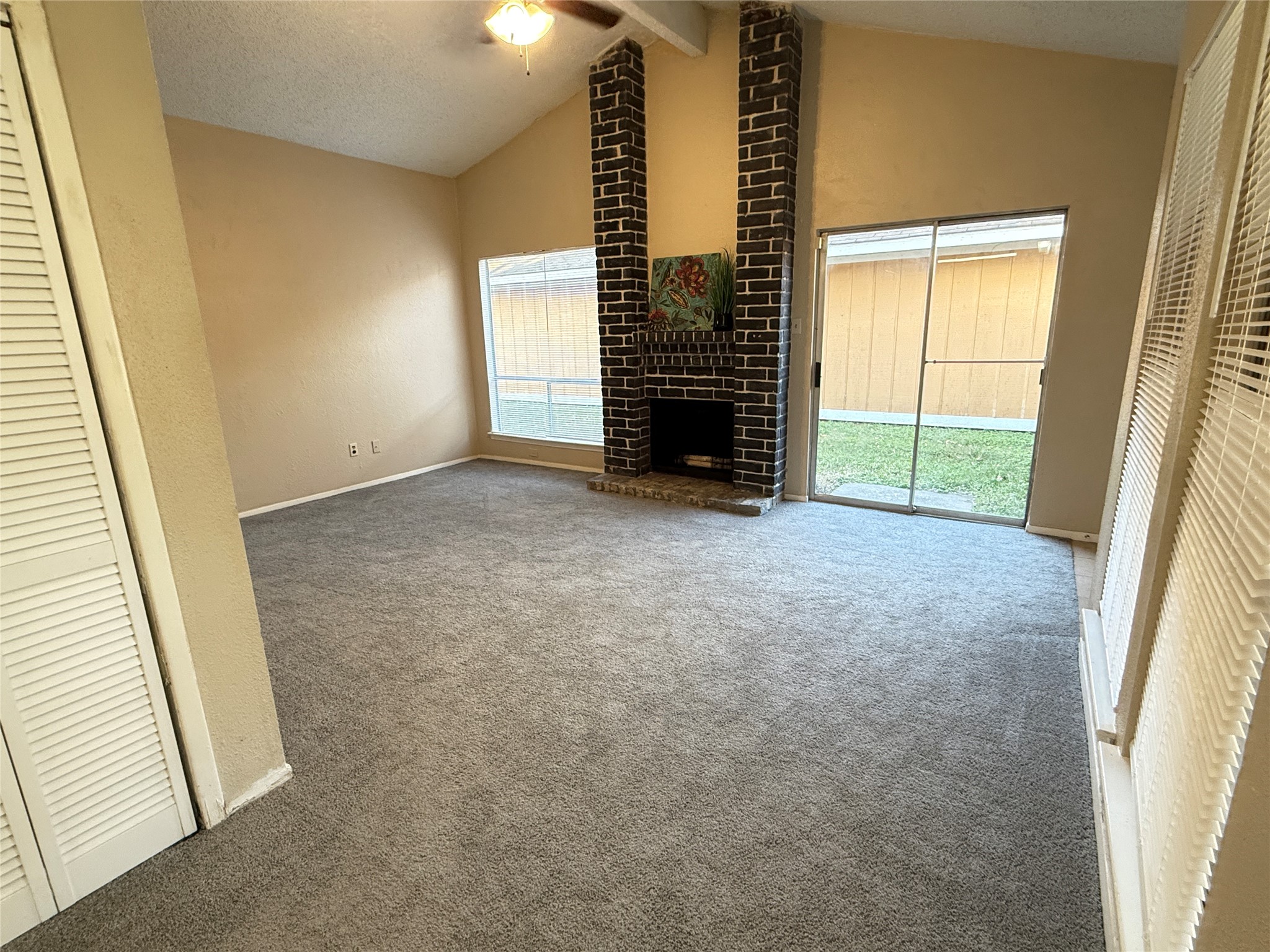 3219 Forestbrook Drive Spring, TX 77373 - Photo 6 of 16 Spacious living room with high ceilings, featuring a cozy brick fireplace. It has large windows and sliding glass doors that offer plenty of natural light and access to the backyard. The room is carpeted, adding warmth and comfort.