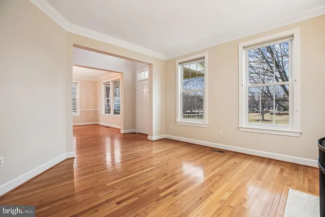 a view of an empty room with wooden floor and a kitchen