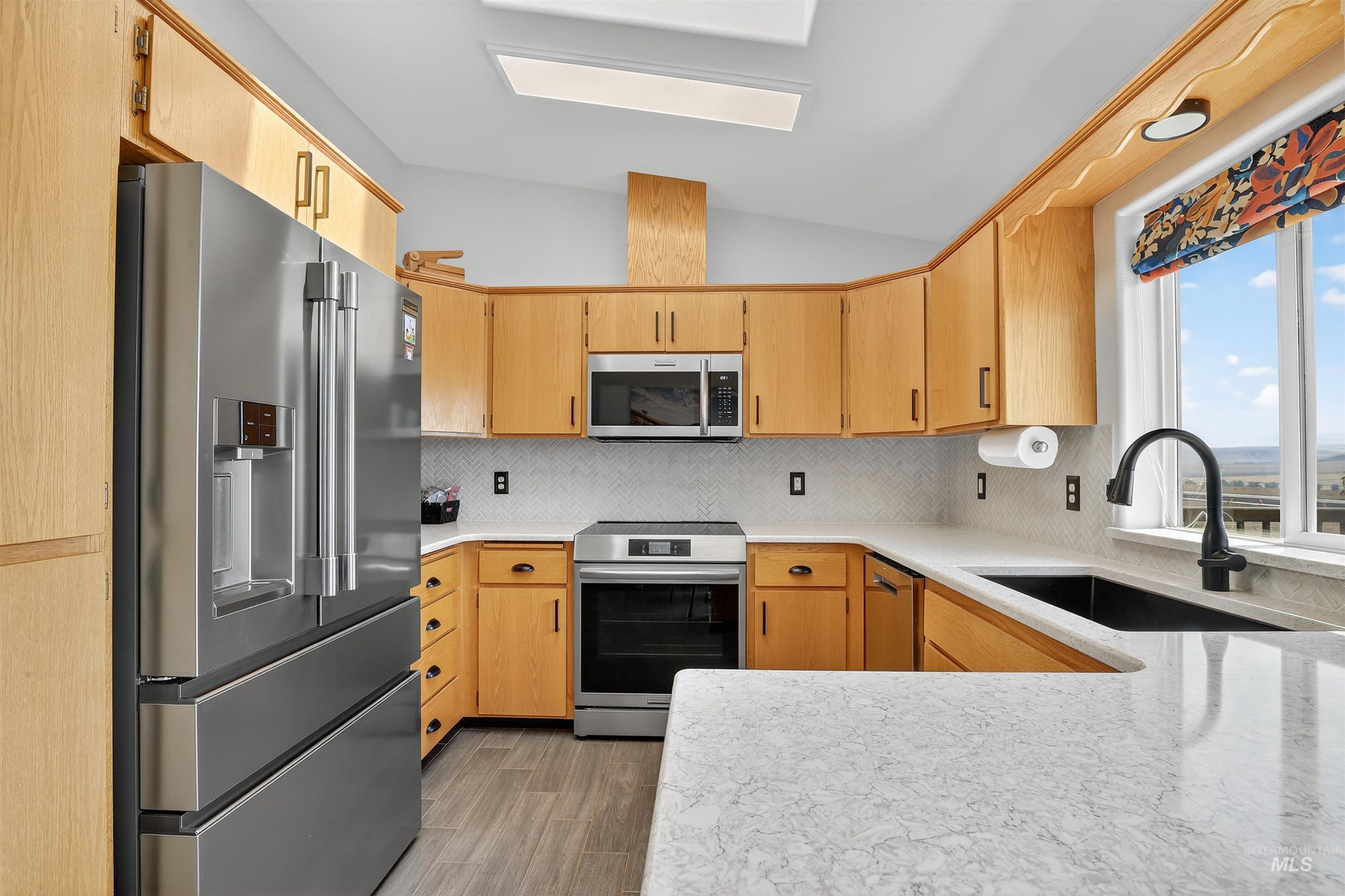 1810 Birch Drive Lewiston, ID 83501 - Photo 7 of 47 Kitchen featuring appliances with stainless steel finishes, decorative backsplash, light stone counters, light wood-style flooring, and light brown cabinetry