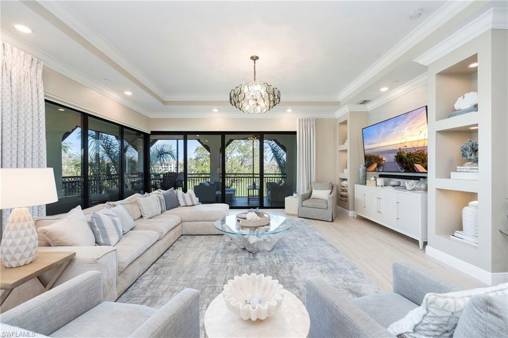 16351 Viansa Way, Unit 202 Naples, FL 34110 - Photo 2 of 35 Living room with built in shelves, a chandelier, a tray ceiling, crown molding, and light wood-style floors