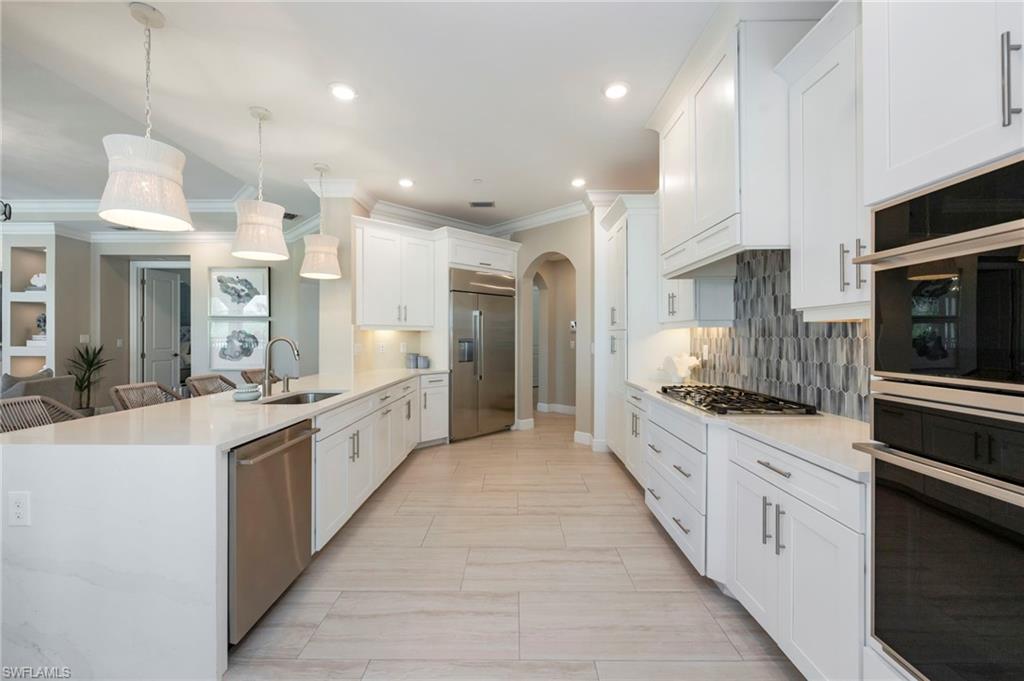 16351 Viansa Way, Unit 202 Naples, FL 34110 - Photo 6 of 35 Kitchen featuring arched walkways, light stone counters, stainless steel appliances, a peninsula, and ornamental molding